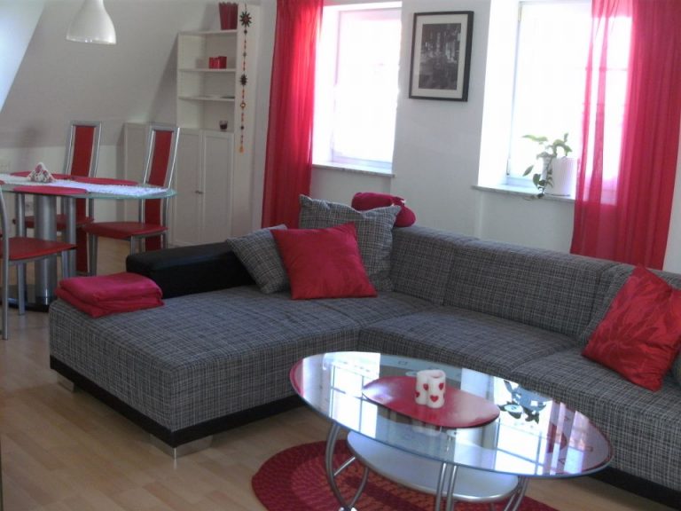 Wohnzimmer mit grauer Eckcouch und roten Kissen
